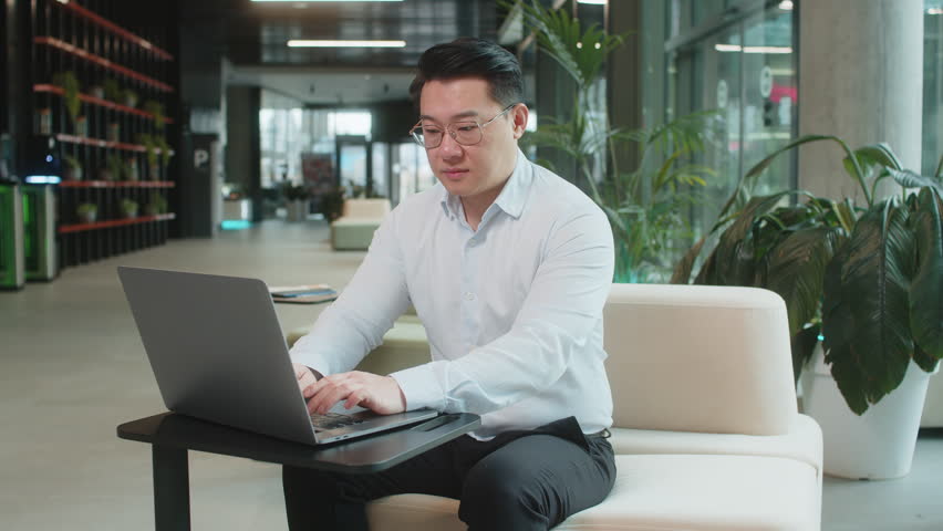 Like. Happy young businessman guy working on laptop looking approvingly at camera showing thumbs up, like sign positive something good, positive feedback sitting in modern office lobby. Businesspeople