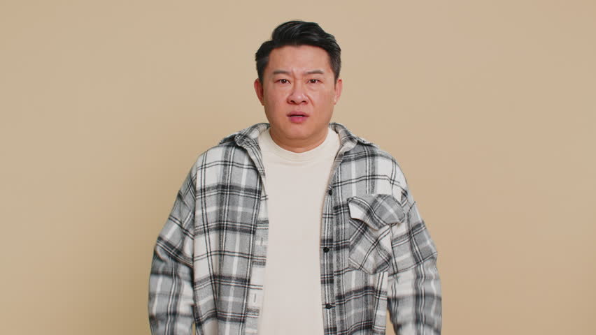 Stressed depressed Asian man terrified about danger problems, suffering phobia, anxiety disorder expresses fear waving no, insecure, stress, panic. Scared fearful guy isolated on beige background