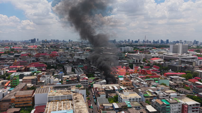 Black smoke rises from a burning building amid the dense cityscape of Bangkok Thailand