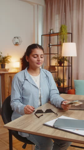 Young businesswoman freelancer putting on party glasses holding fan of cash money euro banknotes showing thumbs up, celebrate, success career, online income, wealth at home office desk. Vertical.