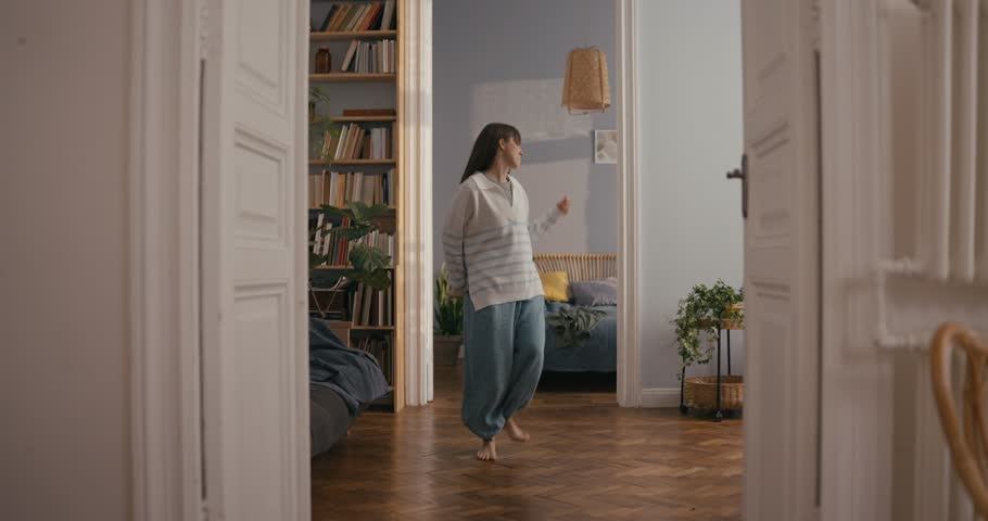 Energetic girl in casual jumps on bed and dances her energetic dance during fun time at home in cozy apartment. Improvisational Fun Dance at Home