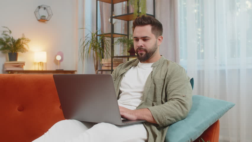 Surprised Caucasian man with brown hair using laptop, receive mail good news message, wow shocked by sudden victory celebrate lottery jackpot win purchases online shopping at home on sofa. Lifestyles.