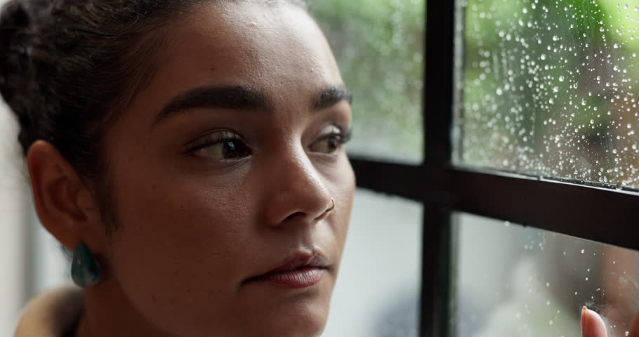 Thinking, woman and worry with window at house for reflection, loneliness and PTSD of storm phobia. Rain, female person and thoughts for winter weather, remember past and anxiety of trauma experience