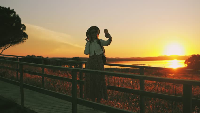 Young woman traveler walk wooden bridge in natural park during sunset, enjoy peaceful landscape with golden light and scenic surroundings, embody carefree travel spirit. Europe travel. Lifestyle,