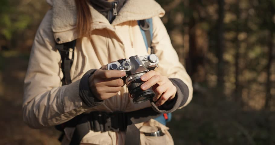 Close up of Girl in hiking clothes holding a camera taking a photo of the view during her hike in the forest. Taking photos while hiking in the forest