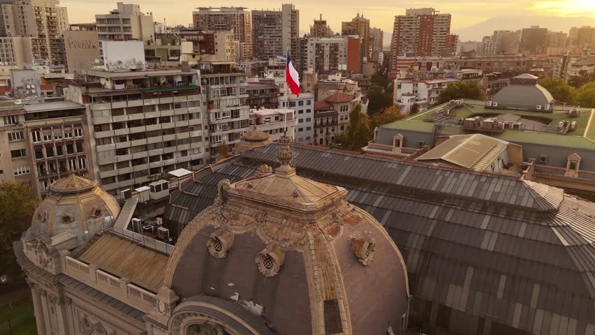 Flag of Chile on top of historic building in capital of Chile. Sunset time. Aerial Orbit shot. Housing area and residential towers in de Chile City. Panorama view.