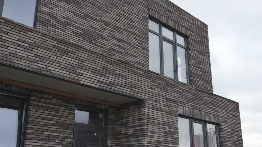 Two-story house with dark brick giving sleek and minimalist appearance. Large windows with black frames add to contemporary style