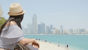 Young pretty tourist woman stands at scenic viewpoint, taking in enjoy stunning Abu Dhabi skyline panorama and beach, reflecting peace, relaxation, and urban beauty in the UAE - Powered by Shutterstock - Get 15% off with code: PIKWIZARD15