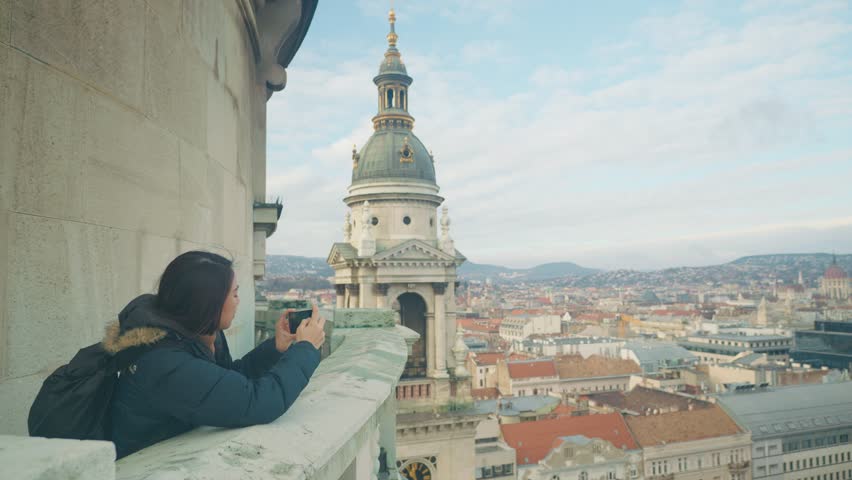 A person captures the breathtaking cityscape from atop a historic tower. The panoramic view showcases urban architecture and distant mountains, perfect for photography enthusiasts and travelers alike.
