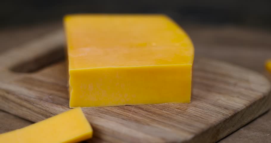 yellow hard cheese cut into long pieces, slicing yellow cheese close-up