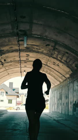 Woman running in a tunnel towards the light. Athlete runs in the tunnel. Active lifestyle.