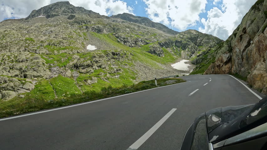 Sharp bends on an alpine road between steep rock faces and green mountain slopes. Picturesque car ride on a summer road trip across Great St Bernard Pass, one of the highest road pass in Switzerland.