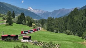 AERIAL: Train travels through a picturesque Swiss alpine valley, passing through pine forests, rustic villages and with views of majestic mountains. Scenic route through the mountainous countryside. - Powered by Shutterstock - Get 15% off with code: PIKWIZARD15