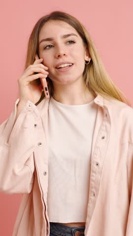 Casual young woman having a phone call, showing various facial expressions and hand gestures on a pink background