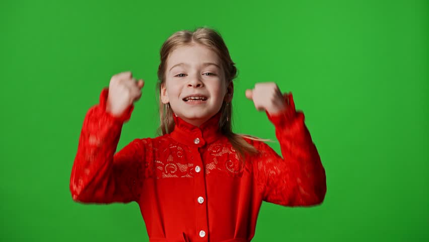 Children emotions advertisement concept. Smiling girl child shows winning gestures and happy positive expression, isolated on chroma key green screen studio background mockup.