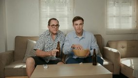 Father and son cheer enthusiastically while watching a sports game on TV, holding beer bottles and popcorn bowl. - Powered by Shutterstock - Get 15% off with code: PIKWIZARD15