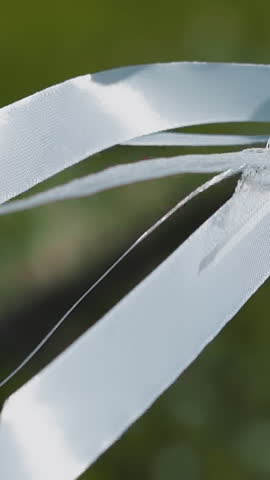 Thin silk ribbons and lace strips of bride dress waving in light wind in sunny summer park closeup slow motion. Elegant wedding ceremony accessories