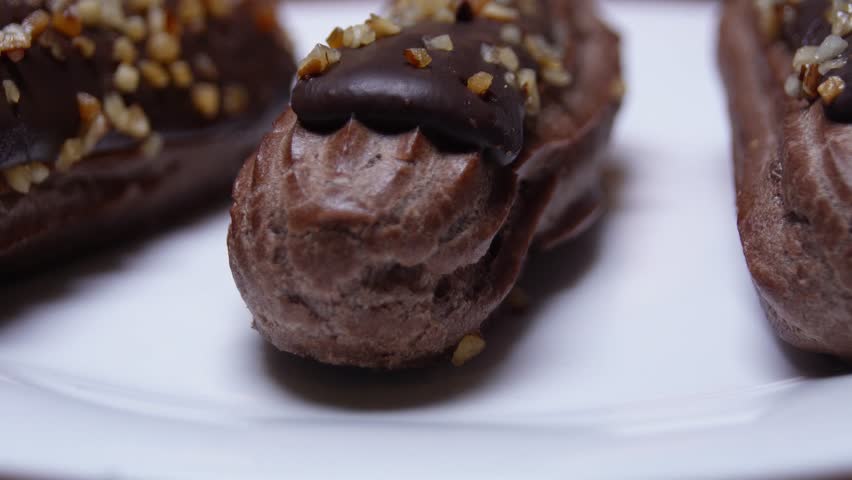 A plate of chocolate covered pastries with nuts on top. The plate is white and the pastries are brown