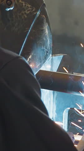 Male labourer with safety mask welds steel carcass in manufacturing workshop close rare view. Employee operates with steel construction at workplace