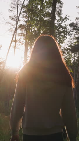 Female walking through dense woods at sunset. Young woman walks alone finding inner peace of mind in nature. Escaping from problems in fresh air