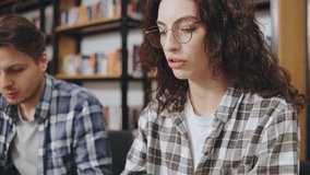 Students studying in a modern library, one focused on a laptop while the other listens to music with headphones, surrounded by bookshelves filled with literature - Powered by Shutterstock - Get 15% off with code: PIKWIZARD15