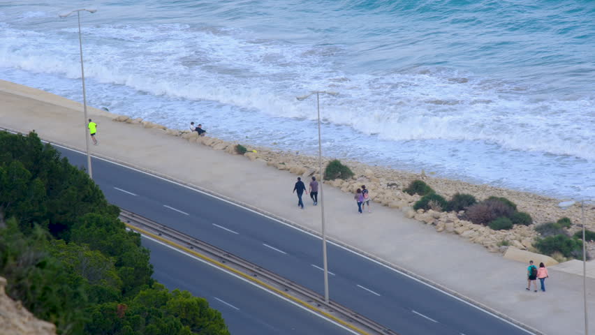 Scenic coastal walkway with people strolling and waves crashing by the shore
