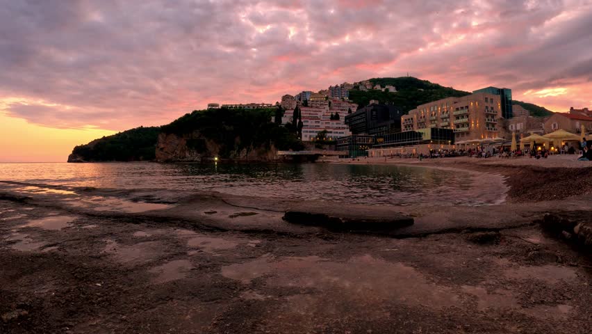 A serene sunset casts vibrant colors over a coastal town in Montenegro, highlighting its unique architecture and peaceful shoreline.