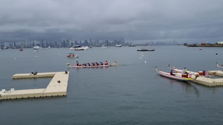 Dragon boat race near floating dock with boats and city skyline in the background under cloudy skies