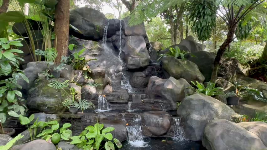 Small flowing refreshing stream with waterfalls among the stones in bright tropical foliage. Garden as nature background