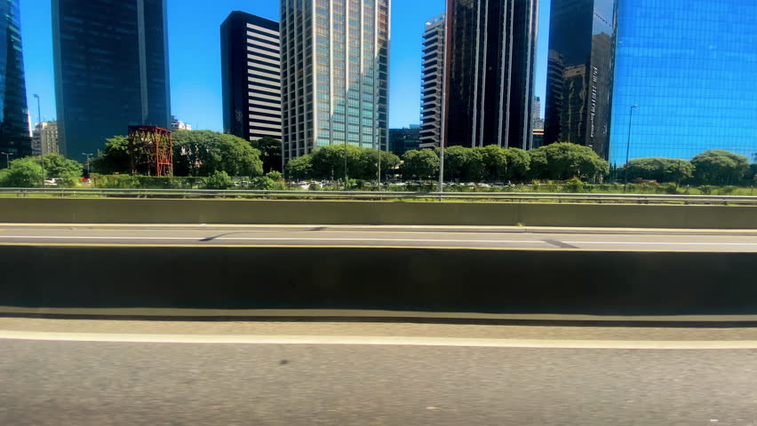Left Side view of a Driving Plate: Car traveling and arriving in Buenos Aires, Argentina. Big buildings, cars, trees in the background.