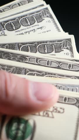 A closeup view of cash, specifically hundreds of dollar bills being held in a persons hand