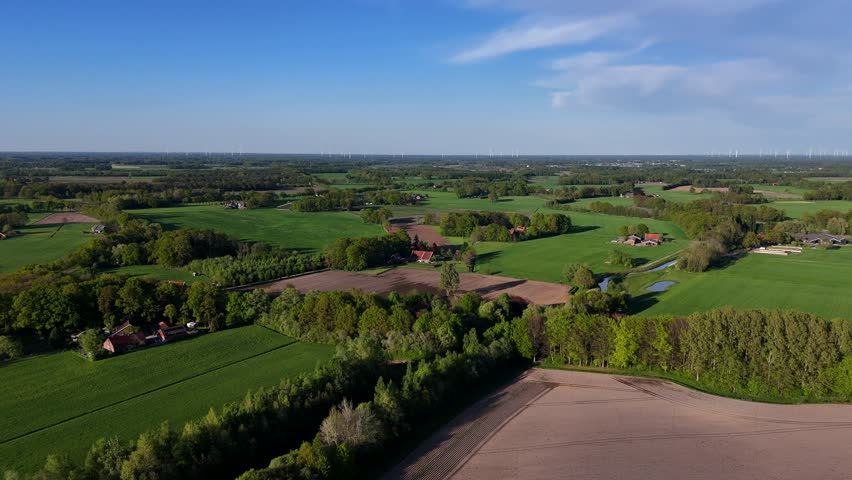 Different colored agricultural farm fields in american with flowing river. Sunset time with blue sky in springtime. Forest trees, suburb neighborhood with farmers house. Aerial wide shot.Drone footage