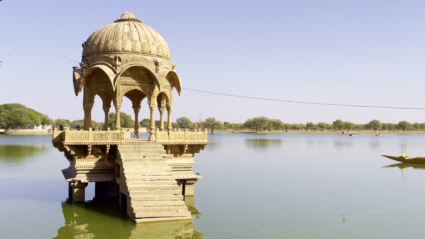 Gadsisar Lake in Jaisalmer sparkles under the Rajasthan sun, mirroring ancient temples and peaceful pavilions. Calm waters, migratory birds, and golden hues enhance its timeless desert beauty India