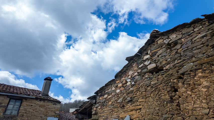 Dynamic timelapse shows an old tiled roof and stone facade under fast-moving clouds, emphasizing historic rural architecture and nature.
