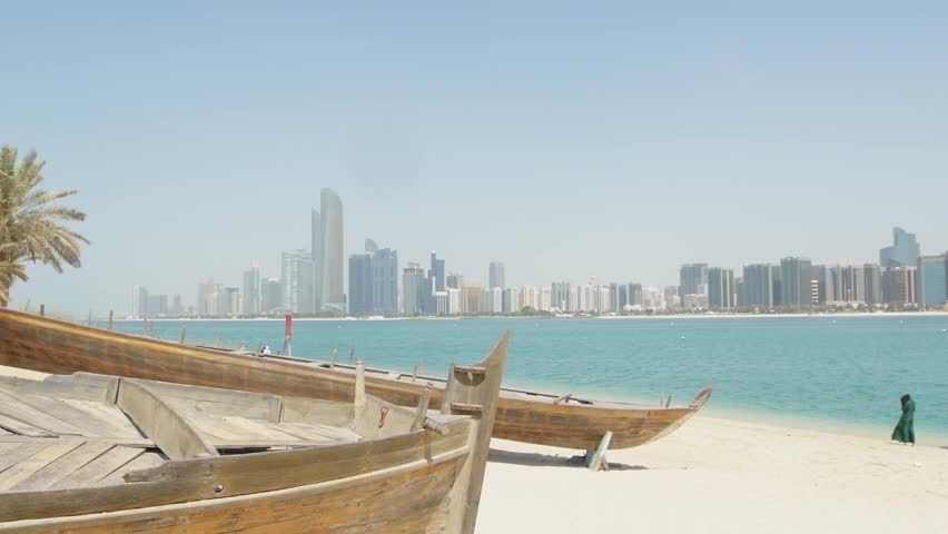Skyline of modern Abu Dhabi and old traditional fishing boats in Heritage Village in Abu Dhabi in United Arab Emirates UAE. Couple tourist enjoy beach and visit sightseeing travel destination in UAE