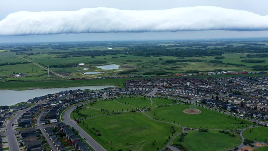 Large cloud looms over a town with houses and a park. The sky is overcast and the atmosphere is somber