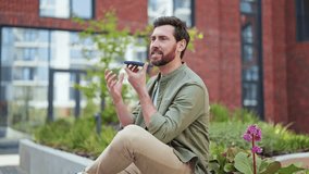 Handsome businessman in casual clothes talking on speakerphone outdoors. Successful man using smartphone in urban space. Positive emotions, relaxed atmosphere. - Powered by Shutterstock - Get 15% off with code: PIKWIZARD15