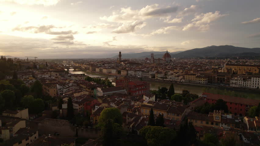 Aerial drone descent from Florence skyline at sunset behind trees, Italy