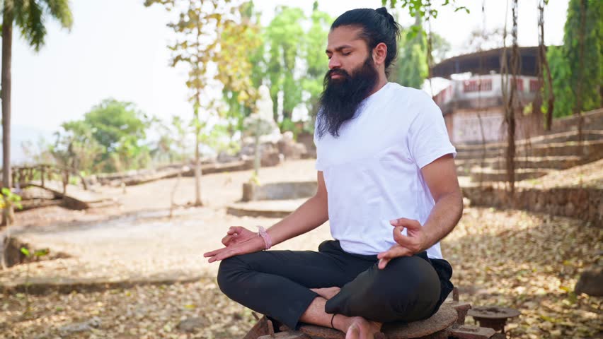 Spiritual follower practices breathwork during yoga, Rugged yogi meditates in lotus position under tree outdoor, Devotee controls breath seated as meditative form, Wellness seeker focus into solitude