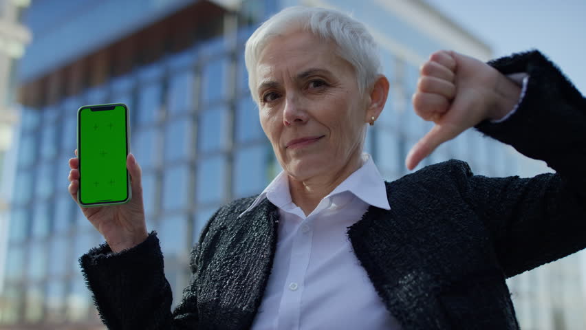 Displeased woman showing green screen phone with thumbs down