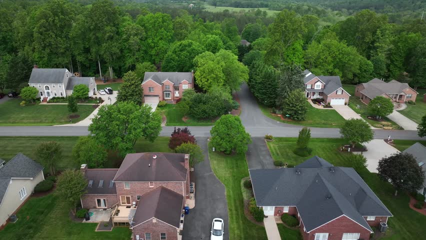 Historic single family houses with large property and green forest trees in spring. Quiet suburb area. Aerial lateral wide shot. Street and driveway at cloudy day.
