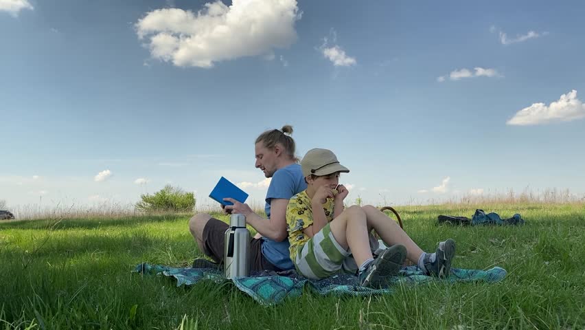 Young dad and son enjoying a summer picnic on a grassland, spending quality time together. They engage in fun outdoor activities, bonding and creating happy memories under the warm sun