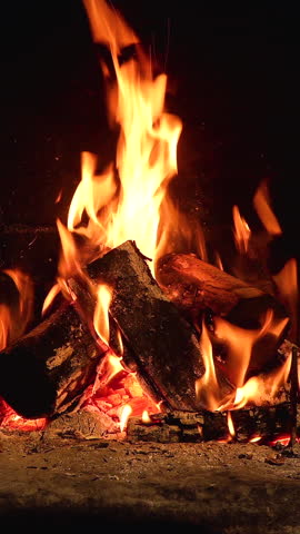 Vertical video of Cozy Fireplace with Burning Logs, A warm fire blazes in a rustic stone fireplace, with glowing embers and vertical flames.