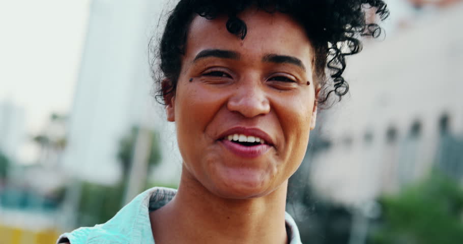 Happy Young African American woman laughing and smiling standing in urban setting close-up face. Portrait of a black latina 20s girl feeling joy, authentic and real life