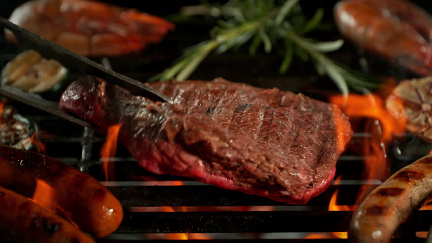 Super Slow Motion Shot of Flipping Beef Steak Meat on Hot Grill with Flames at 1000fps.