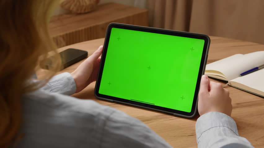 Woman sit desk use digital tech tablet with green screen mock up. Hand scroll ipad web site, swiping like photos. Girl hold pad close up. Chroma key page. Cozy home background. Online app copy space.