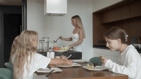 A mother lovingly prepares and serves delicious pancakes while her three happy daughters enjoy eating them together at the dining table. Warm family moments and bonding in a contemporary home kitchen. - Powered by Shutterstock - Get 15% off with code: PIKWIZARD15