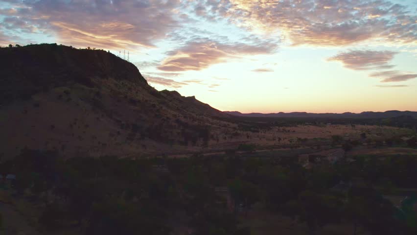 Rising drone footage of the MacDonnell Ranges near Heavitree Gap, Alice Springs, Mparntwe, with late afternoon behind the range. Northern Territory, Australia. August 2022.