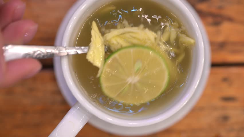 Warm ginger tea with lemon slowly stirring in white ceramic cup, resting on wooden surface, embodying relaxation and wellness moments