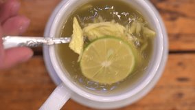 Warm ginger tea with lemon slowly stirring in white ceramic cup, resting on wooden surface, embodying relaxation and wellness moments - Powered by Shutterstock - Get 15% off with code: PIKWIZARD15